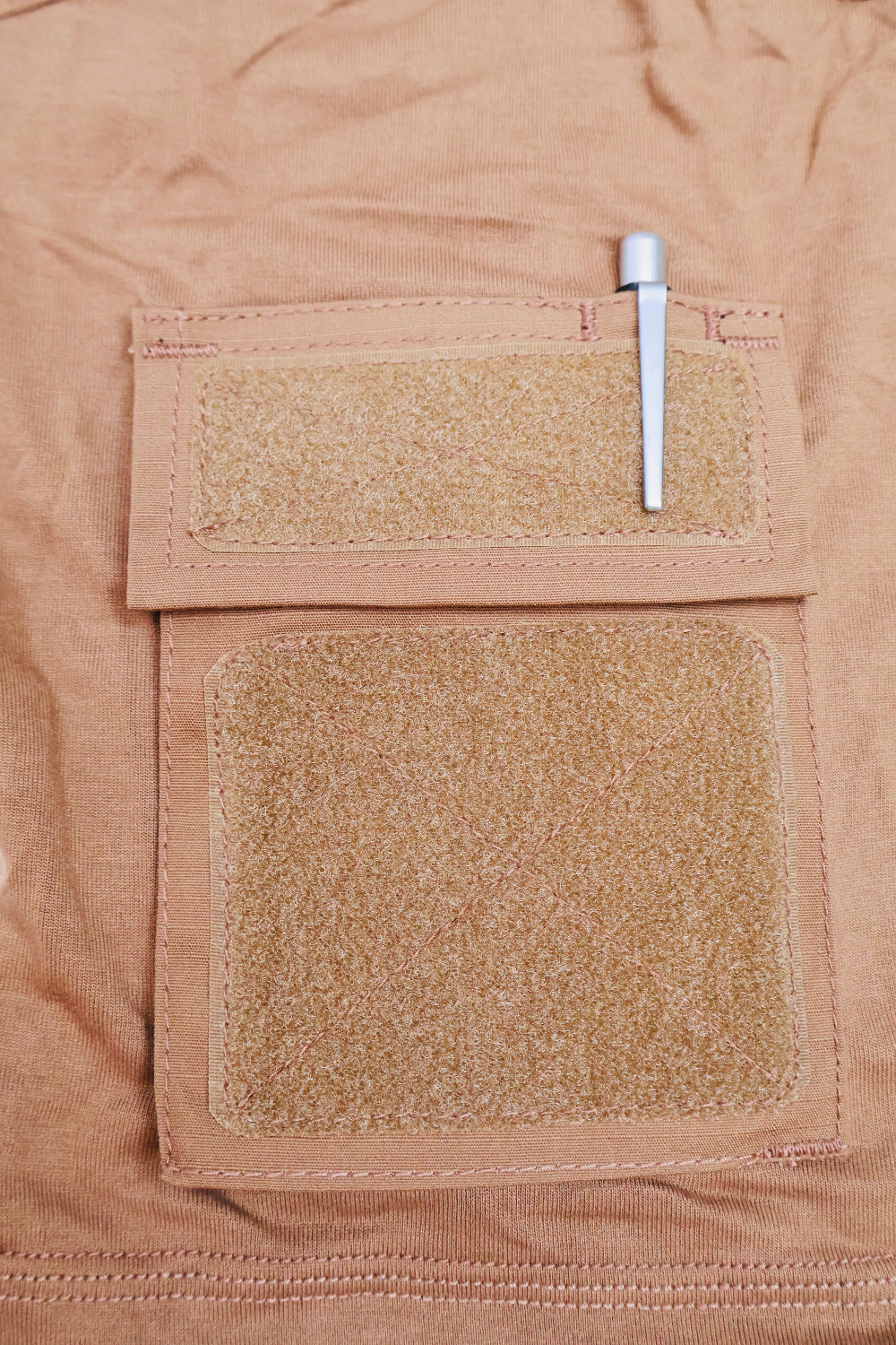 Close-up of a tan fabric pocket with two patches and a pen on a matching background