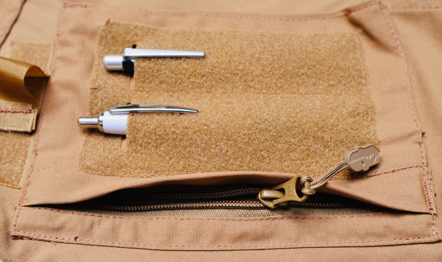 Close-up of a brown tactical pocket with various components attached.